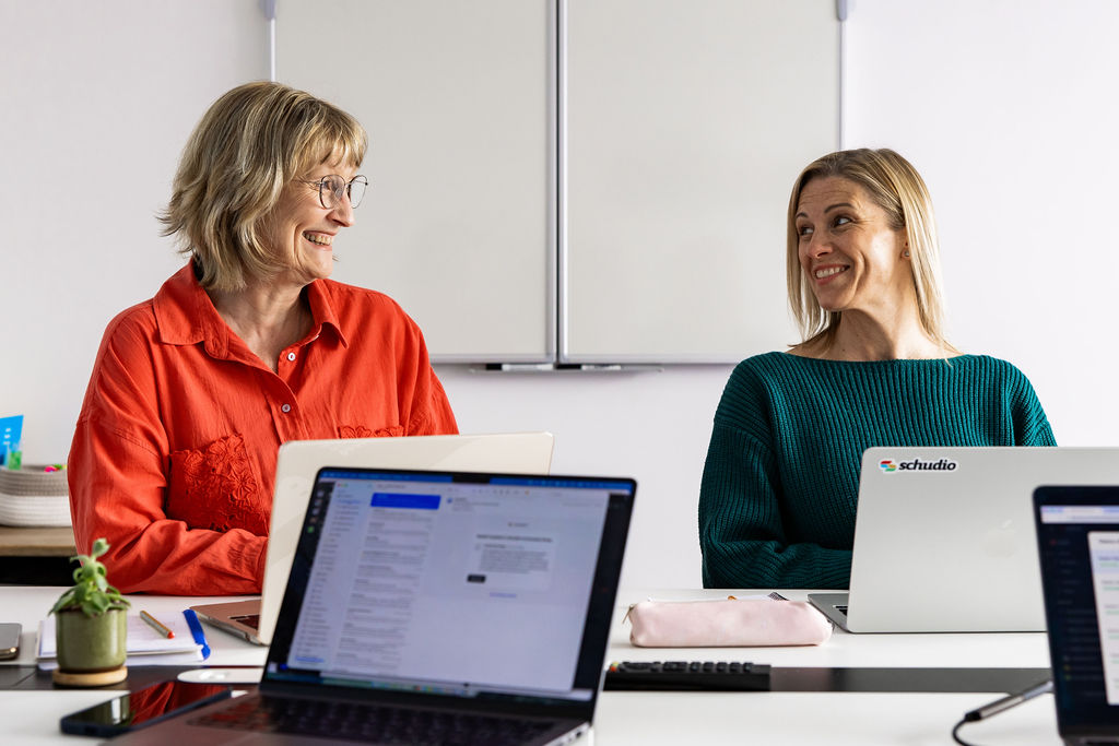 Two Schudio colleagues at their desks, mid-conversation